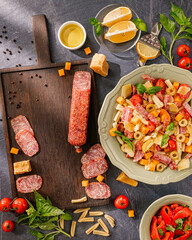 italian pasta salad with salami, cheese cubes, fresh basil, sweet peppers, cherry tomatoes, olive...