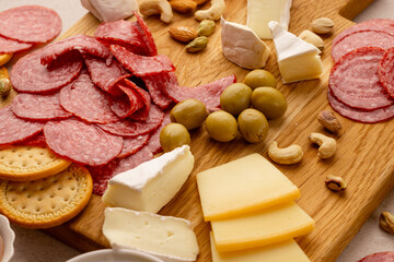 close-up charcuterie board with thinly sliced salami, round crackers, brie, hard cheese slices, mixed nuts and green olives on wood, festive gourmet appetizer, rustic daylight party snack