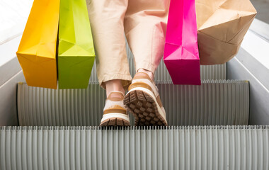 Woman legs in sneakers in shopping mall with bags on escalator going up close-up