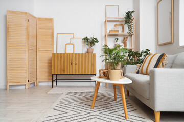 Cozy sofa, coffee table and chest of drawers with blank posters in interior of living room