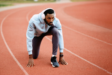 Athlete with headphones preparing to start running on track