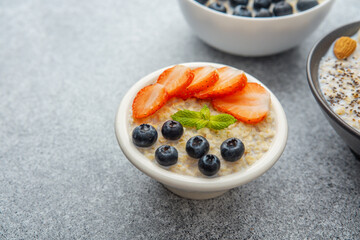 Oatmeal porridge with strawberries blueberries and mint in white bowl