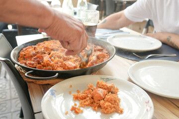 A man is eating food from a large bowl on a table. There are two plates and two cups on the table