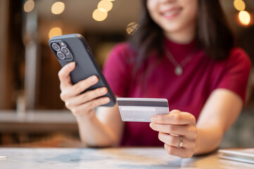 Close up of asian woman looking at smartphone and holding credit card on marble table in the cafe.