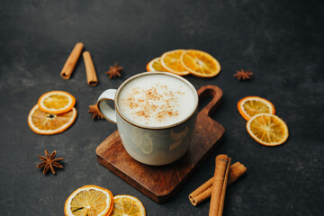 Warm beverage with foam, cinnamon, star anise and dried orange slices on dark background.