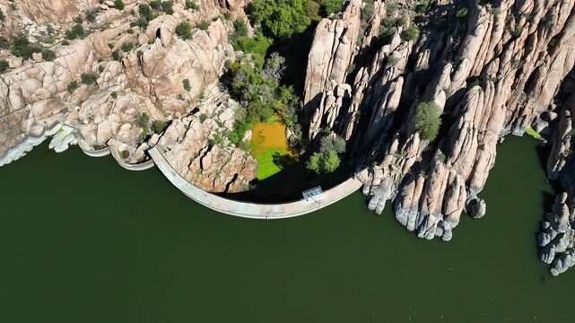 Aerial view of Watson Lake's dam contrasting with the rugged, rocky terrain and lush green trees, creating a scenic landscape, Watson Lake, Arizona, United States.