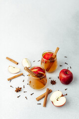 Warm apple cider drinks with cinnamon sticks and anise on light surface with apple slices