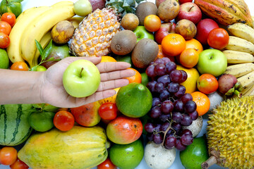 Mixed exotic fruits background for nutrition theme. hand holding a green apple.