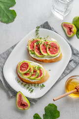 Sweet toasts with fresh figs, cheese, thyme, and honey on a light background.