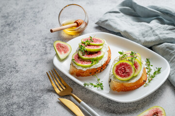 Sweet toasts with fresh figs, cheese, thyme, and honey on a gray background close up.