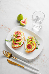 Sweet toasts with fresh figs, cream cheese, thyme, and honey on a marble background.