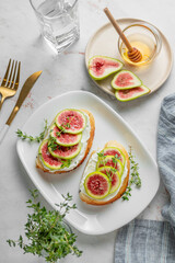 Sweet toasts with fresh figs, cream cheese, thyme, and honey on a marble background.