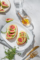 Sweet toasts with fresh figs, cream cheese, thyme, and honey on a marble background.