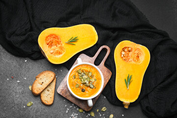Butternut squash soup with bread and pumpkin seeds on dark background with rosemary.