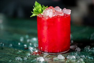 Refreshing red cocktail with crushed ice and mint garnish in a clear glass on a rustic green wooden...