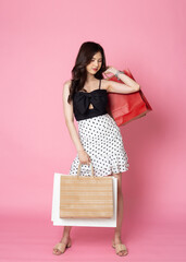 Young Asian Woman looking at camera while holding shopping bags on pink background