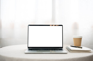 Fototapeta premium White screen laptop aside notebook with pen and coffee cup on round table in a cafe or living room.