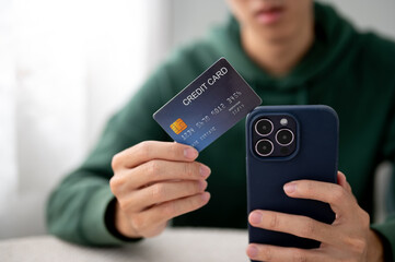 Close up of a man holding or showing credit card as looking at phone while sitting at table in cafe.
