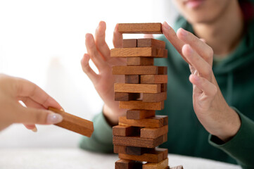 Close up man's hands putting a wooden block on top in tower building game while playing with friend