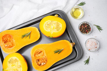 Butternut squash halves with rosemary, peppercorns, salt, and oil on a baking sheet