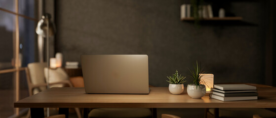 Laptop and books with potted plants and lamp on wooden table aside window in a living room or office