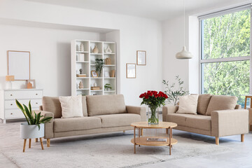 Interior of stylish living room with grey sofas and beautiful red roses on coffee table