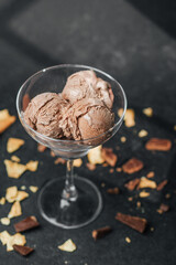 Glass cup with scoops of chocolate ice cream and waffle crumbs on dark surface