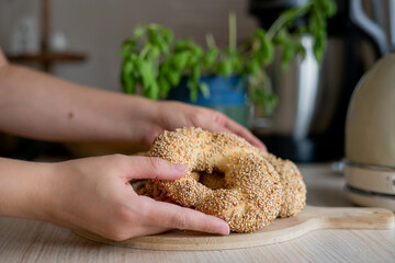 Closeup of female hands holding hot homemade Turkish simit in the kitchen. Bagels with sesame seeds. Pastry.