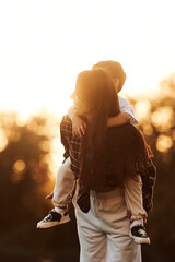 On the back of woman, sunset time. Mother and son together in an open field during daytime
