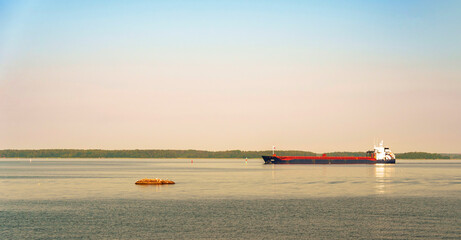 Cargo ship sailing on calm sea near coast at sunset