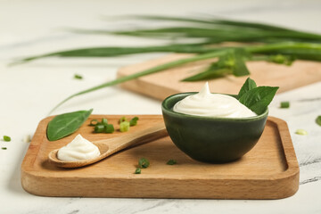 Cutting board with bowl and spoon of tasty sour cream and fresh basil on white marble table