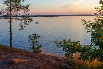 Rocky lake shore with trees and calm water at sunset