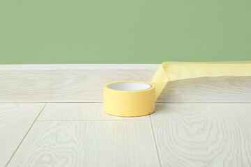 Roll of masking tape on floor near masked baseboard, closeup