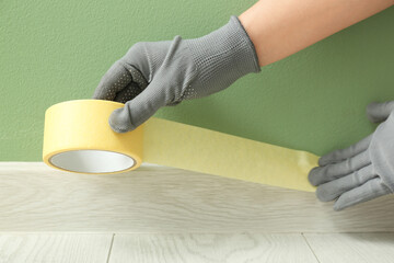 Decorator applying masking tape to baseboard near green wall, closeup