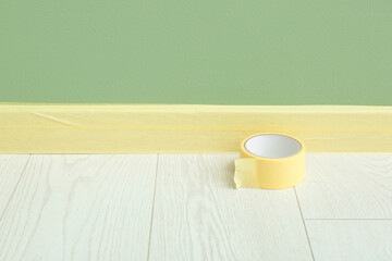 Roll of masking tape on floor near masked baseboard, closeup