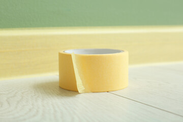 Roll of masking tape on floor near masked baseboard, closeup