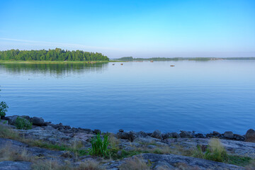 Rocky lake shore with calm water and forested island in morning light