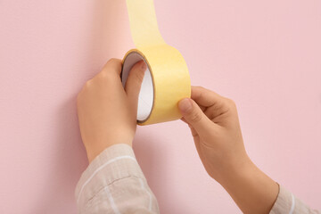 Woman applying masking tape to pink wall, closeup