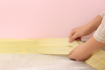 Woman applying masking tape to baseboard near blue wall, closeup