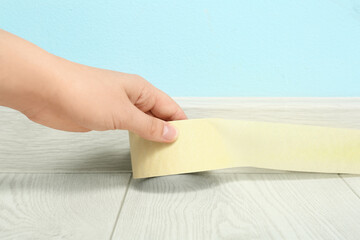Woman applying masking tape to baseboard near blue wall, closeup