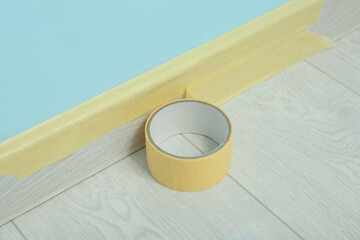 Roll of masking tape on baseboard near blue wall, closeup