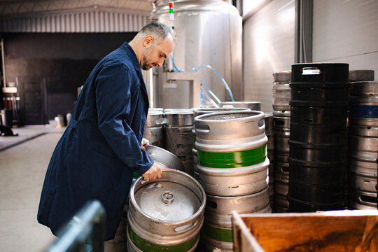 Brewery worker stacking empty beer kegs in warehouse