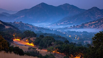 Hilly landscape bathed in twilight, with road lights and foggy valleys beneath distant mountains