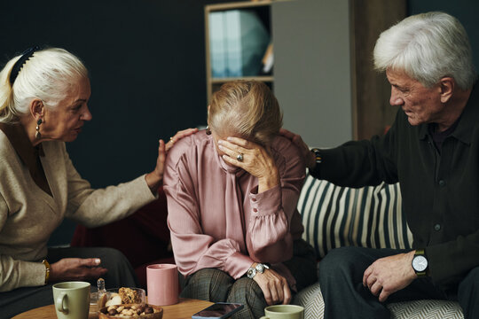 Senior Caucasian woman sitting with head in hand being comforted by male and female friends, supportive couple consoling during emotional moment