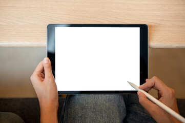 Close up of hands holding stylus writing or drawing on white screen tablet at wooden table in a cafe