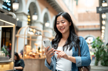 Asian woman holding and looking at phone while walking or standing in shopping mall or indoor market