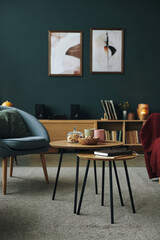 Modern living room interior featuring wooden coffee tables with snacks, mugs, and book on carpet, bookshelf with vinyl records and speakers, abstract art hanging on dark green wall © DragonImages