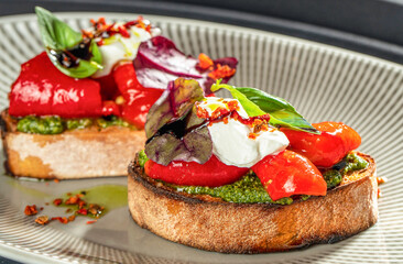 Bruschetta with roasted red peppers, pesto sauce, and creamy cheese topped with basil and herbs on toasted bread
