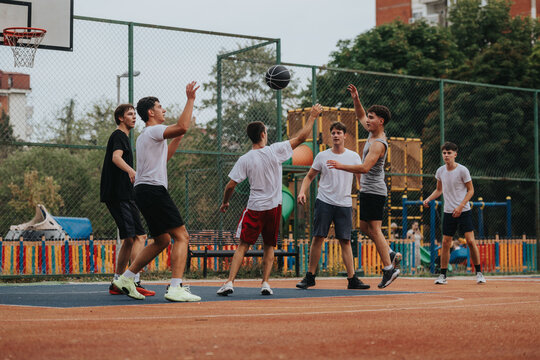 A group of friends playing basketball on an outdoor court, showcasing teamwork and energy in a casual urban setting with a colorful fence and playground in the background.