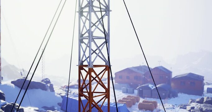 A tall metal tower stands prominently against a snowy background, surrounded by wooden structures and rocky terrain. The winter scene conveys a remote and chilly atmosphere.